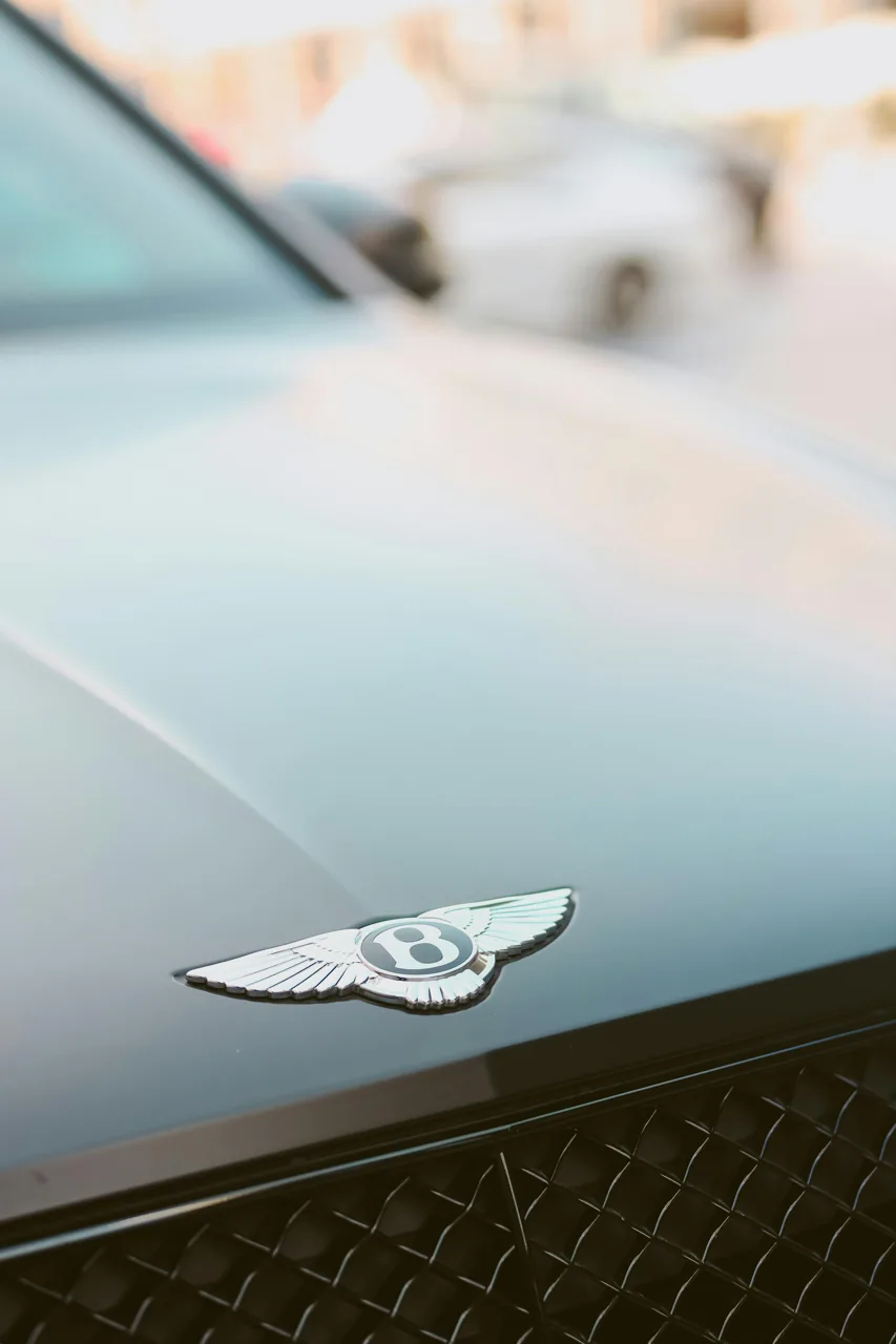 Close view of a Bentley badge on blue-grey paintwork