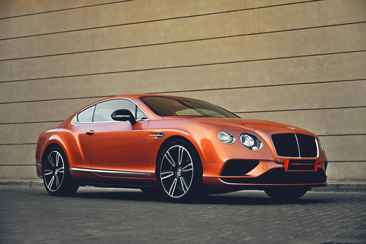 Orange Bentley coupe parked beside a stone wall
